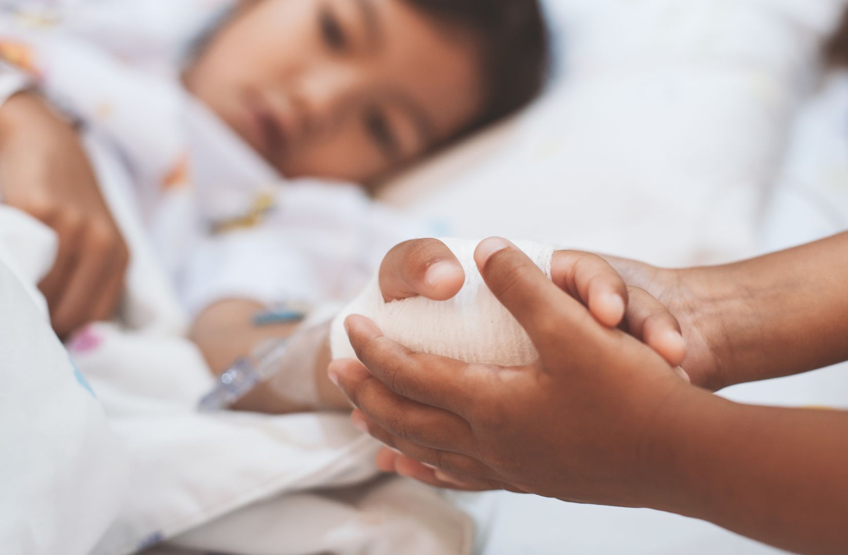 Young girl laying in hospital bed with someone holding her hand